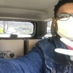 Lachelle E with mask on in a car with food bank boxes in backseat