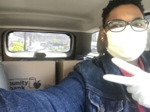Lachelle E with mask on in a car with food bank boxes in backseat