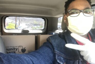 Lachelle E with mask on in a car with food bank boxes in backseat